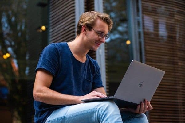 Giovane uomo seduto all’aperto mentre lavora al laptop, simbolo delle nuove professioni digitali accessibili senza laurea.