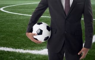Uomo in giacca e cravatta a bordo campo con pallone da calcio
