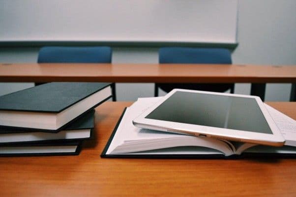 Libri e tablet su un banco in aula, simbolo di formazione continua tra studio tradizionale e digitale.